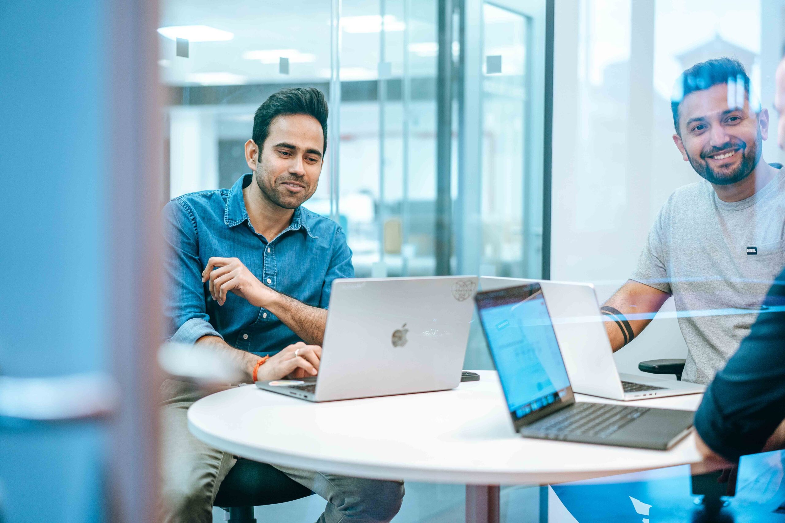 Two colleagues working at their workstations within a glass-panelled office space.